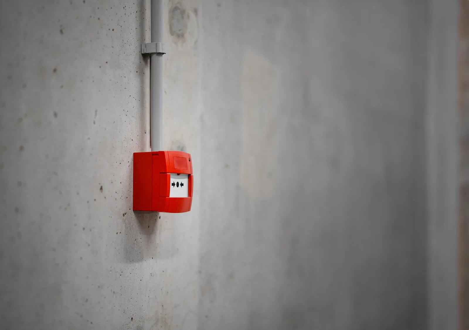 Red manual fire alarm device and conduit on a concrete wall