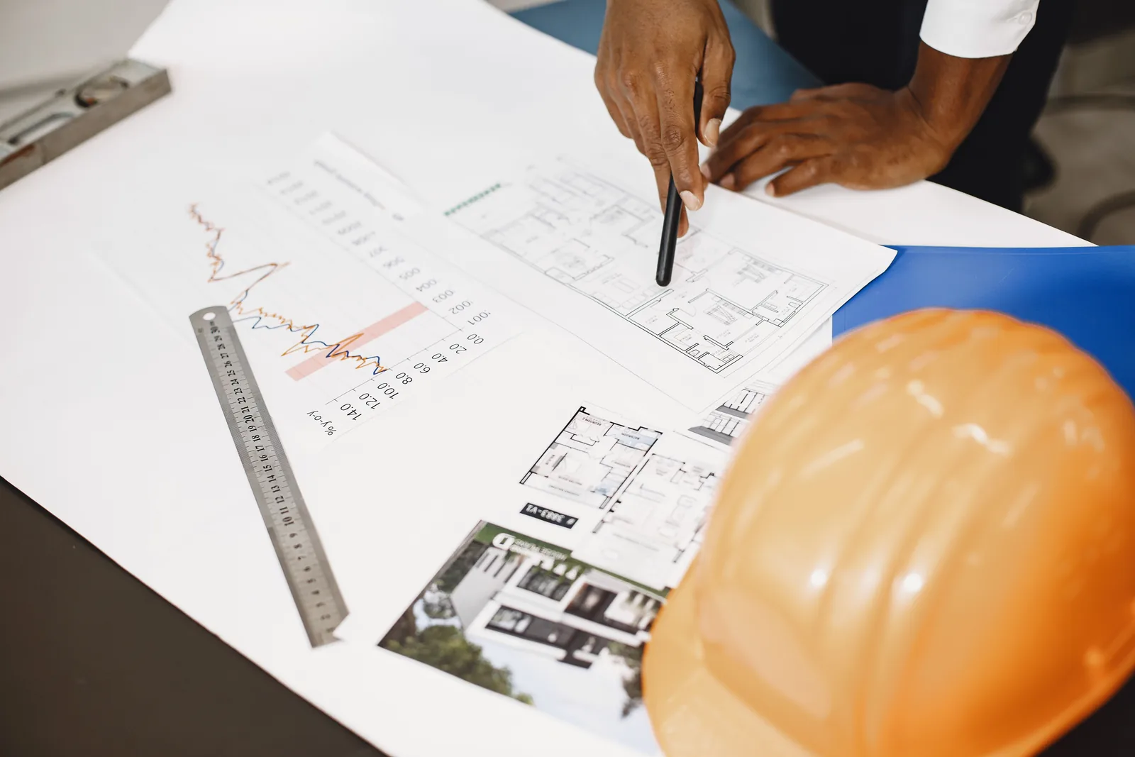 Hands reviewing building plans beside a hard hat